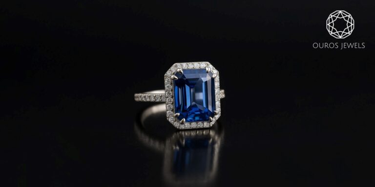 How Ouros Jewels Is Setting the Standard for Contemporary British Jewellery Ouros Jewels emerald-cut blue sapphire ring with diamond halo and pavé-set white gold band.